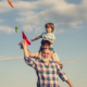 Grandpa standing in front of older son, son has grandson on his shoulders while Flying Kites, Illustrating Estate Planning