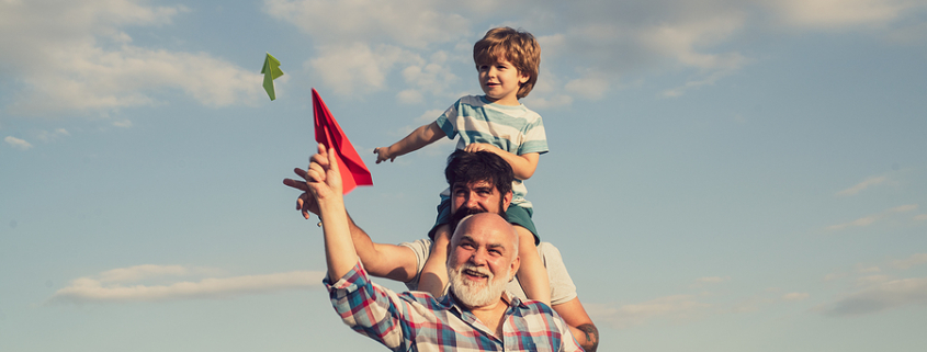 Grandpa standing in front of older son, son has grandson on his shoulders while Flying Kites, Illustrating Estate Planning