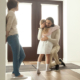Child embraces father at front door of home while mother watches, moving out after divorce, custody arrangements