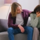 Couple sitting on therapy couch after husband's infidelity. Man with arm around woman, woman has head in hands.