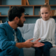 Father talking with daughter, father squatting near sofa girl sits on, comforts her during divorce. How to Support Your Children During Divorce