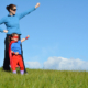 Superhero Guardian and child against a dramatic blue sky background with copy space. Concept photo of super hero girl power play pretend childhood imagination. Guardian For My Child