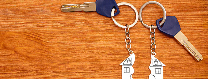 Two keys with split house matching keychains on a wooden table. Splitting assets in a divorce. mortgage