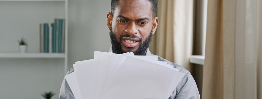 Angry frustrated African American man ethnic bearded businessman boss manage papers looking at documents mistake disappointed with paperwork business trouble startup project problem sitting in office. divorce papers
