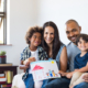 Proud parents showing family painting of son sitting on sofa at home. Smiling mother and father with children?. Black boy with his family at home showing a painting of a happy multiethnic family. blended