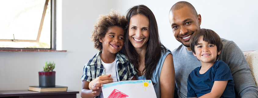 Proud parents showing family painting of son sitting on sofa at home. Smiling mother and father with children?. Black boy with his family at home showing a painting of a happy multiethnic family. blended