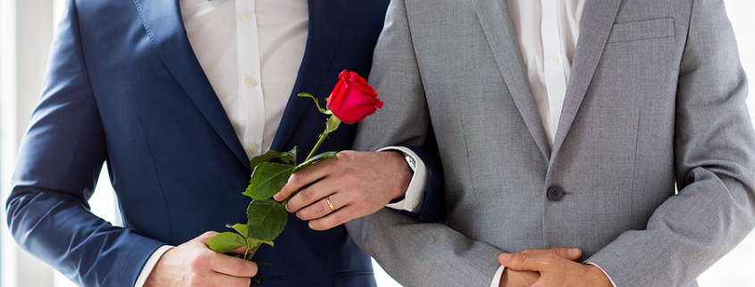 people, homosexuality, same-sex marriage and love concept - close up of happy male gay couple with red rose flower holding hands on wedding. LGBTQ+ Couples