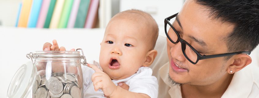 Father holding baby on his lap who is grabbing a jar filled with coins highlighting the best way to leave money to your children.