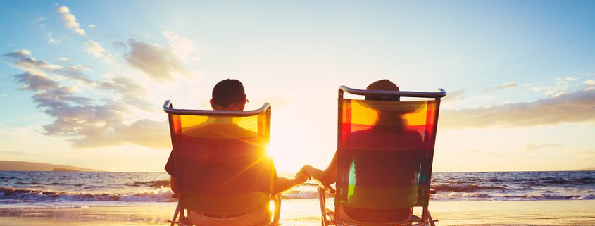 An elderly couple sitting on the beach, smiling and enjoying their retirement, reflecting on their well-protected savings.