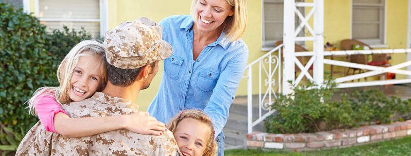 A military father in uniform embraces his smiling family at home, illustrating the intersection of military life and family law challenges.