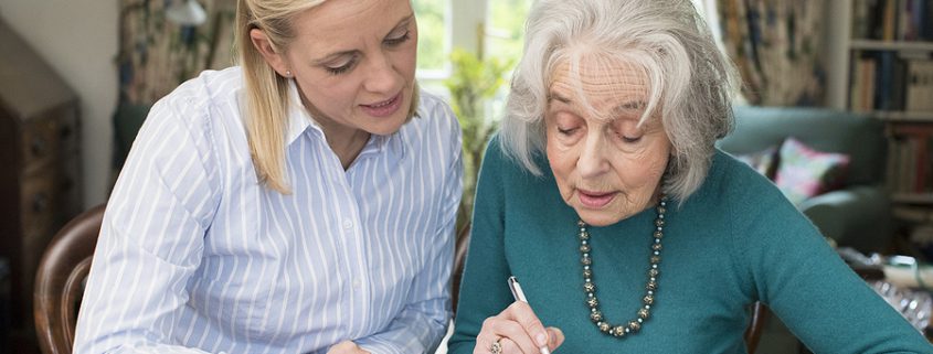 A mature woman assists a senior neighbor with paperwork, symbolizing the importance of guardianship in ensuring proper decision-making support.