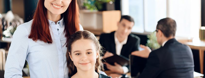 A joyful red-haired woman hugs a smiling young girl in a lawyer's office, symbolizing support and care during a Guardian ad Litem case.