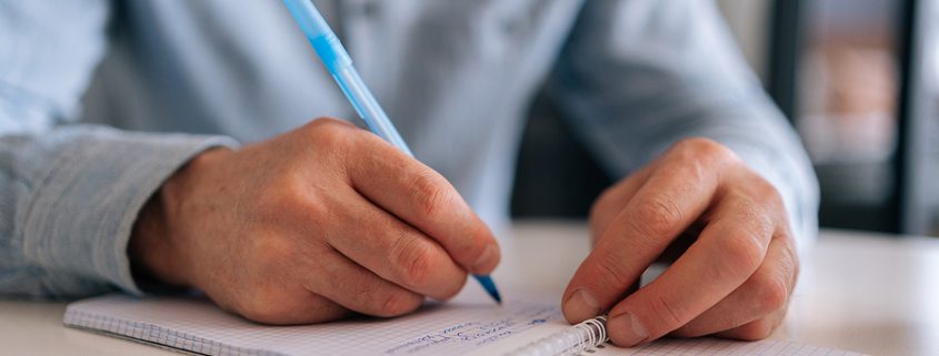 A close-up of a mature male hand signing a handwritten document, highlighting the importance of legally binding agreements and estate planning.