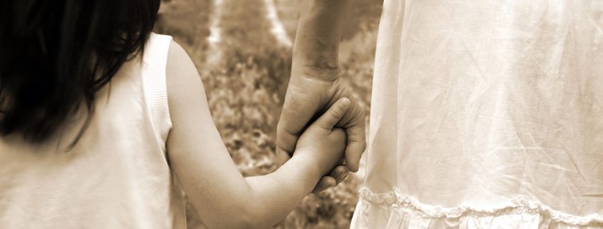 Mother holding her daughter's hand while walking down a path, symbolizing love, guidance, and the mother-child bond.