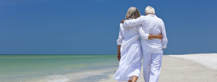 Aging gracefully: A senior couple walks hand in hand along a tropical beach, enjoying the peaceful ocean view and golden sunset.