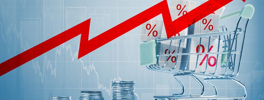 Shopping cart with coins and percentage cubes symbolizing rising costs and inflation.