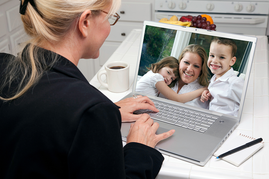 Woman in kitchen using laptop for video call, highlighting family dynamics across distances.