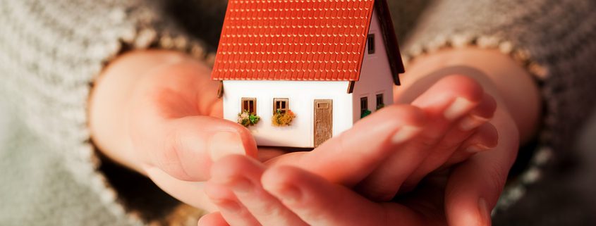 Woman holding a small house model in her hands, symbolizing life insurance trusts, financial protection, and secure future planning.
