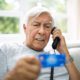 Elderly man on the phone looking worried with a laptop and bills on the table, symbolizing financial fraud and elder abuse.