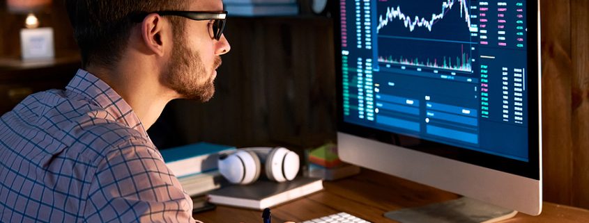 Serious businessman analyzing stock market charts and cryptocurrency data on a computer monitor in a modern office setting.