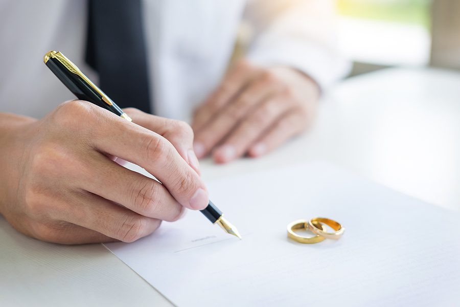 Man signing a legal petition form related to annulment or marital agreement at a desk with documents and pen.