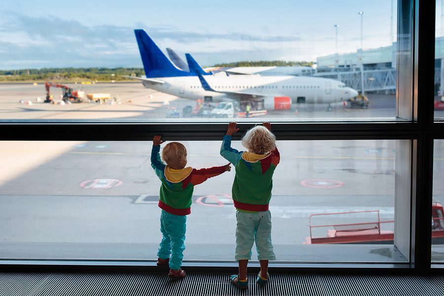 Kids traveling at an airport with an airplane in the background, representing family relocation and expatriate estate planning considerations.