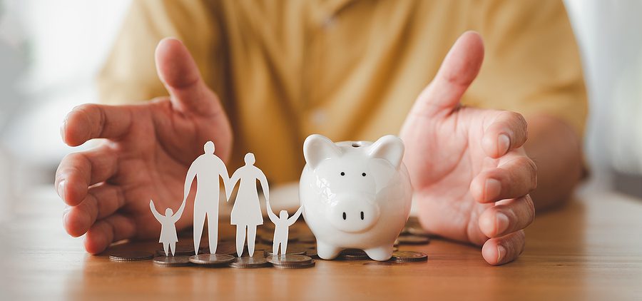 Hands protecting a piggy bank and paper family figures, representing trusts, estate planning, and protecting family wealth.