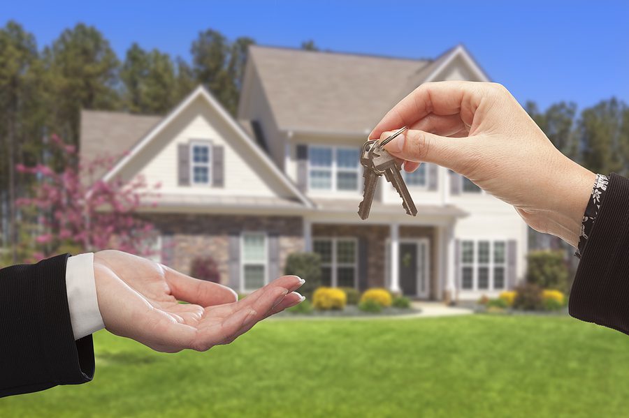Real Estate agent handing over house keys to a new homeowner in front of a beautiful home, representing a successful property purchase and ownership transfer.