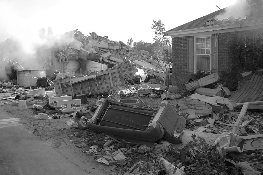 Broken house damaged by a natural disaster with debris scattered around the property.