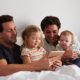 Two dads relaxing in bed with tablet and kids, an example of nontraditional family estate planning